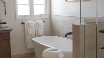 A bathroom with a bathtub, a wooden stool, a window with curtains, and a framed picture on the wall.