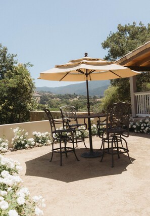 Un patio exterior con mesa y sillas, una sombrilla y vistas del paisaje.