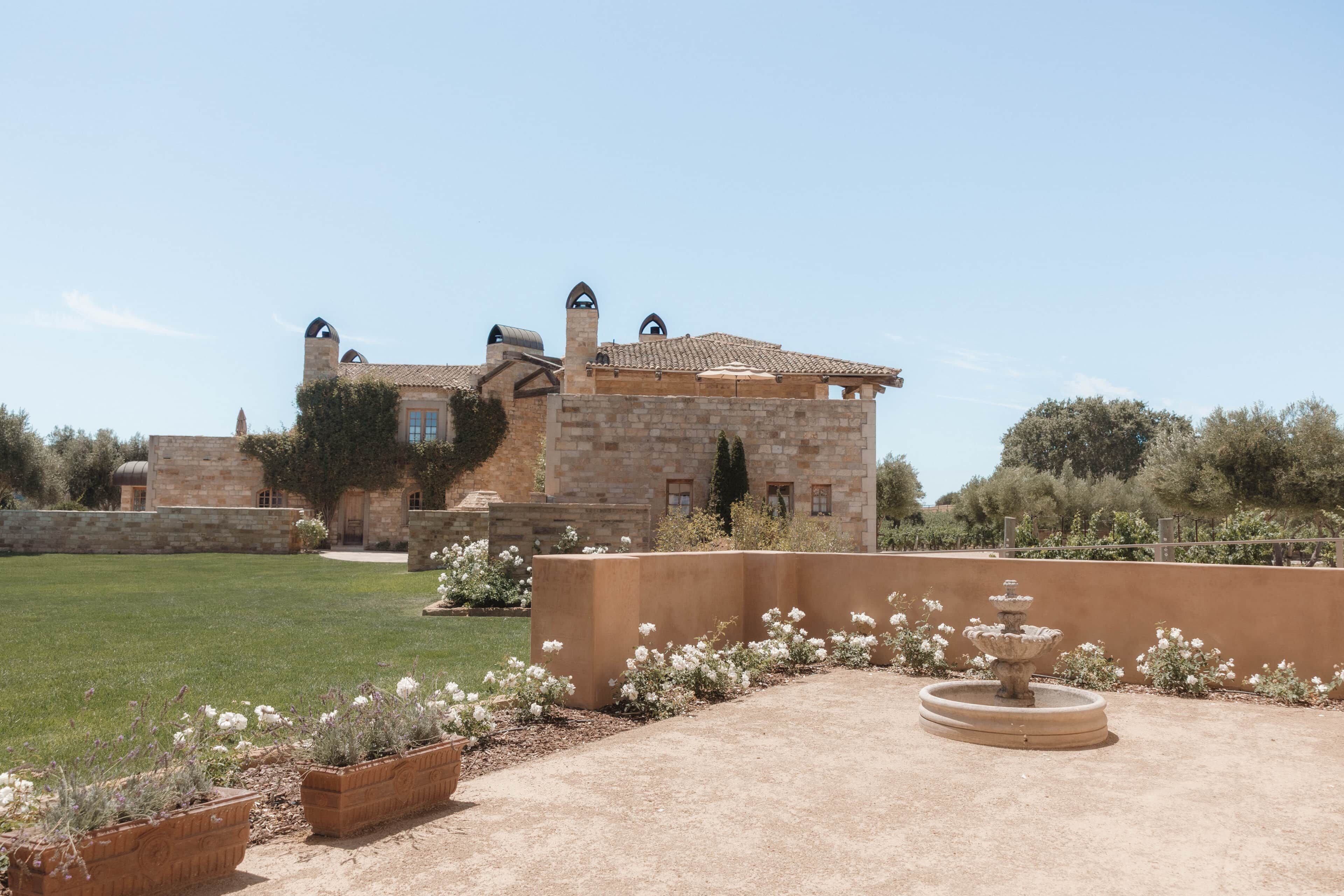 Un bâtiment en pierre doté d’une cour, d’une fontaine et d’une pelouse bien entretenue.