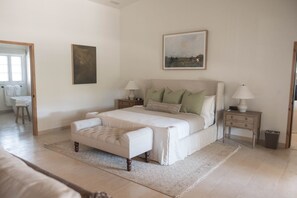 A bedroom with a large bed, two bedside tables, a nightstand, a chair, and a window.