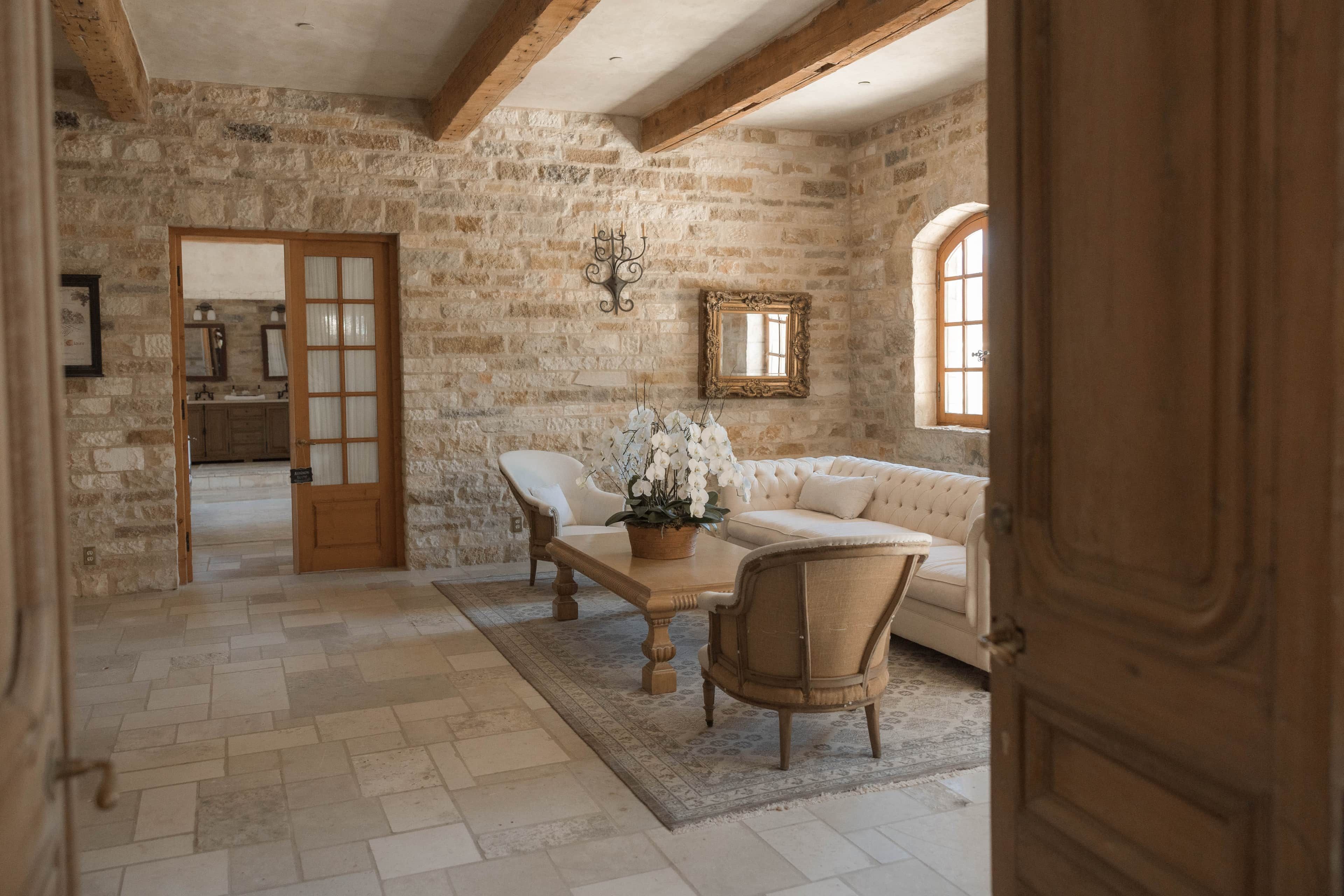 A rustic room with exposed stone walls, a wooden door, a white sofa, a wooden table, and a potted plant.