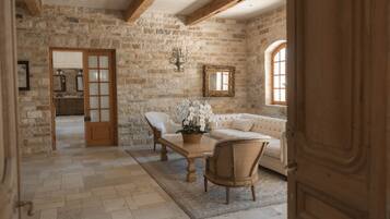 A rustic room with exposed stone walls, a wooden door, a white sofa, a wooden table, and a potted plant.