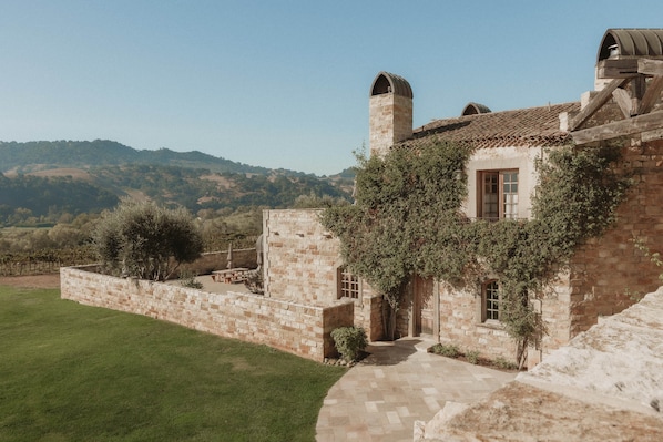 A stone building with a garden, a paved pathway, and a view of the hills.