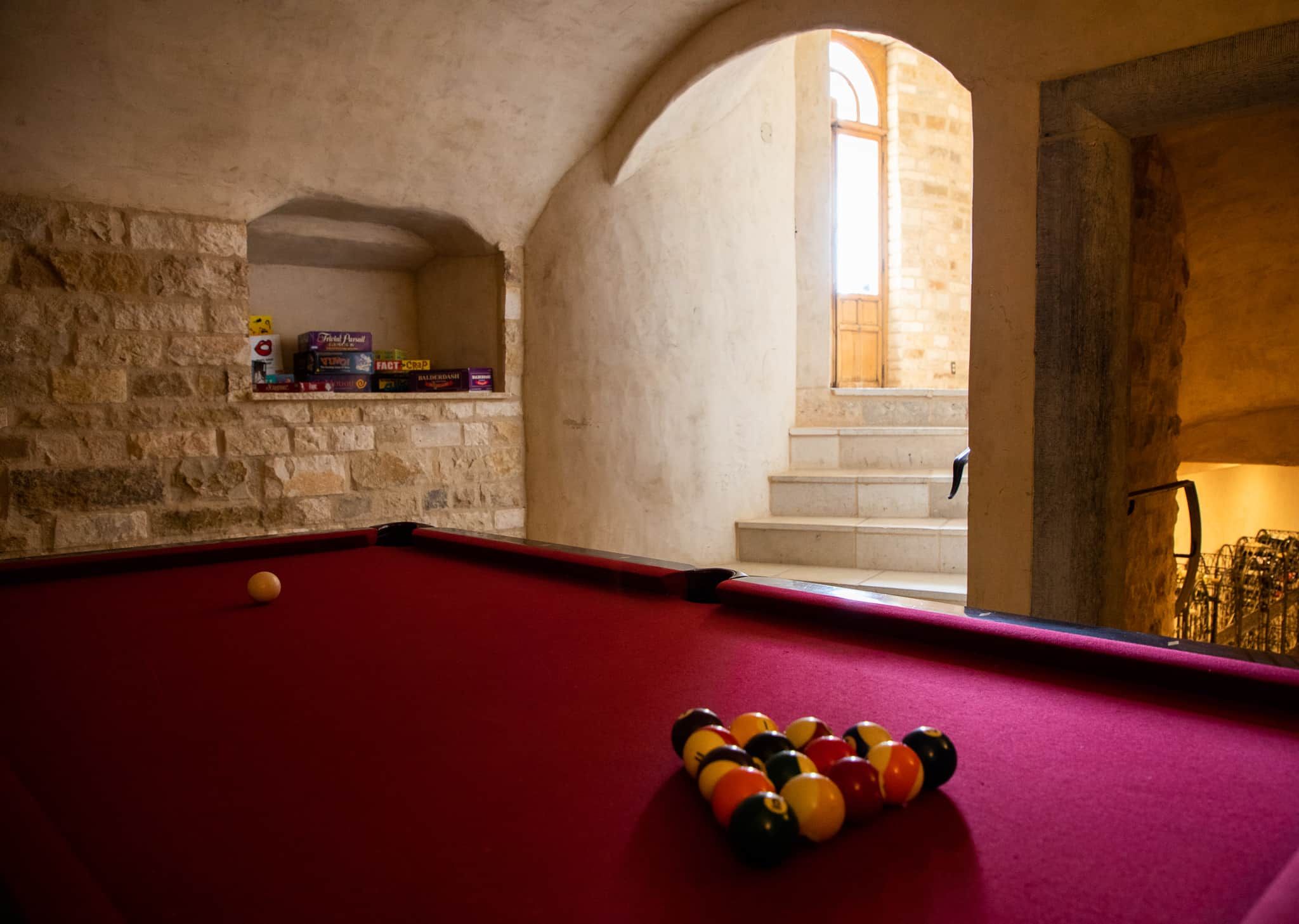 A pool table with balls in the foreground and a stone wall with a shelf in the background.