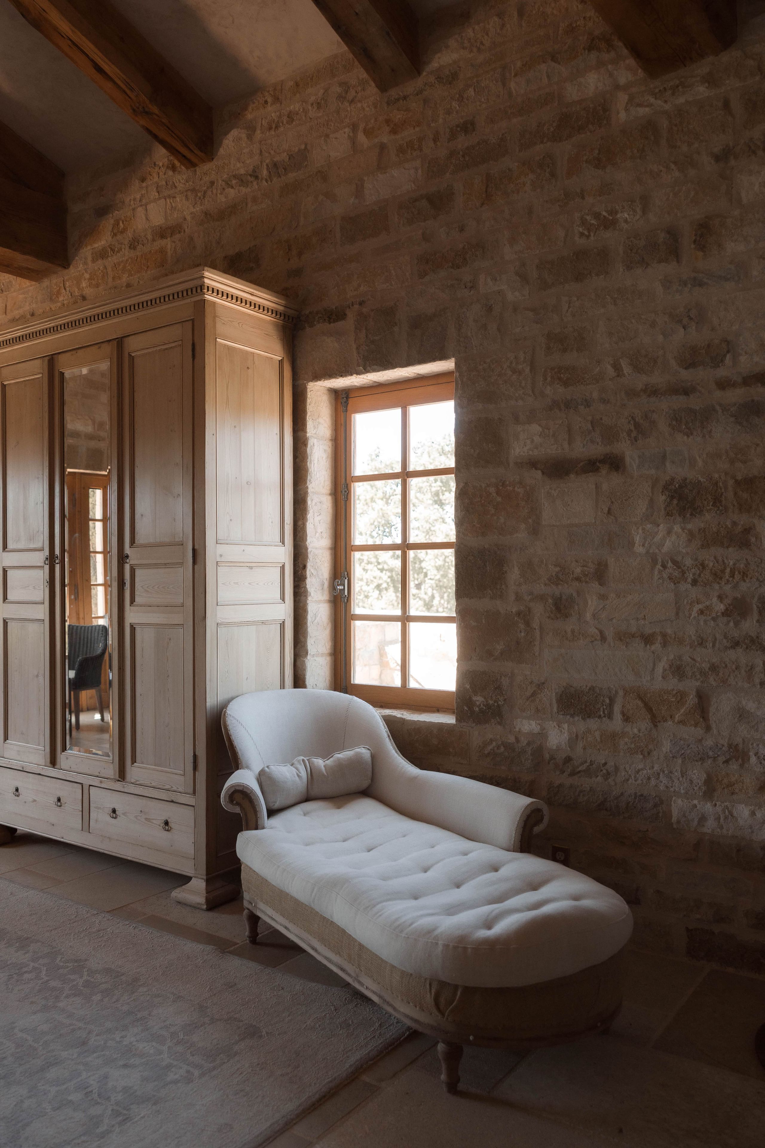 A room with a stone wall, a large mirror, a wooden wardrobe, and a white sofa.