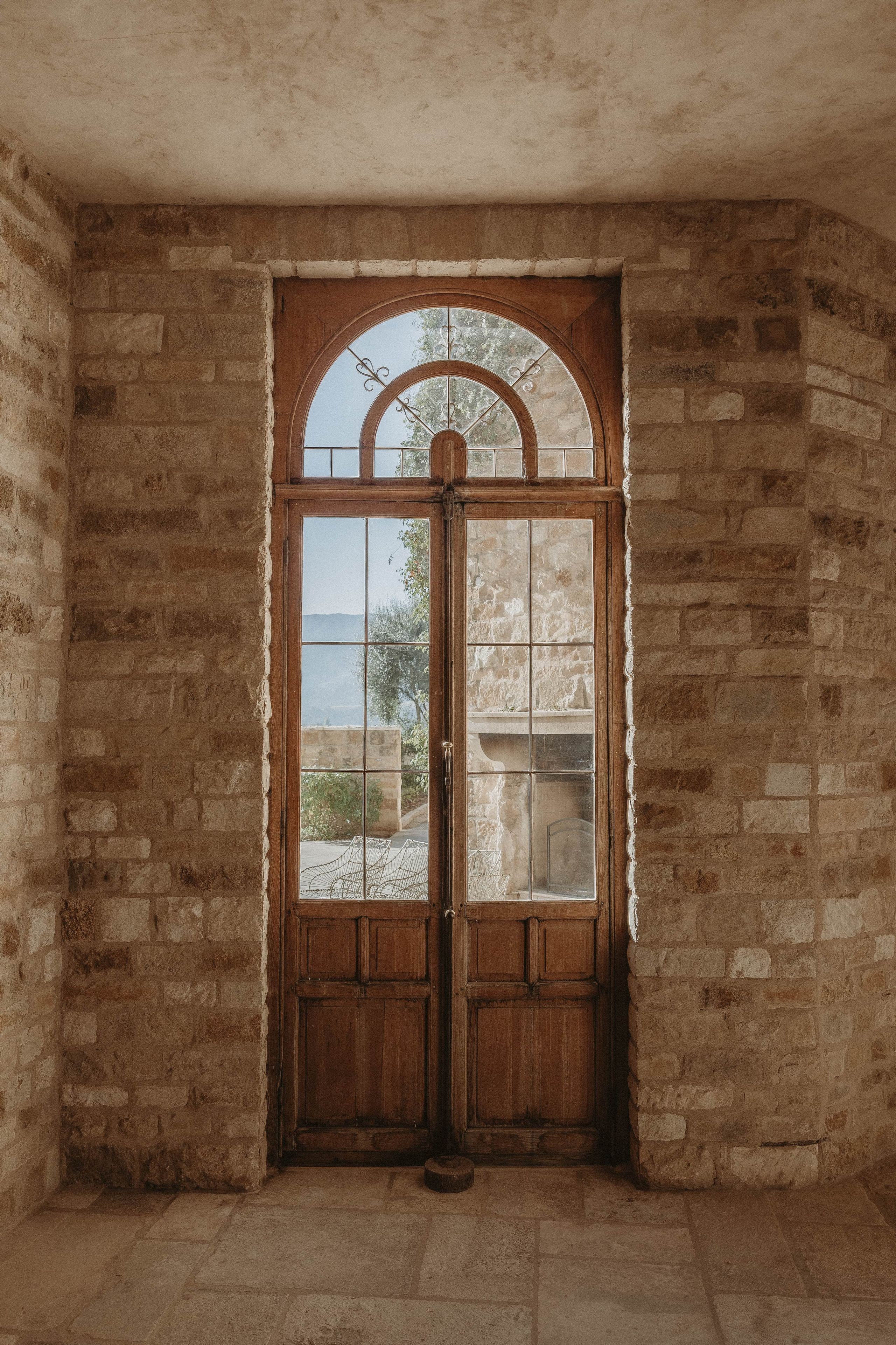 Une porte en bois avec un panneau de verre, encastrée dans un mur de pierre, donnant sur un paysage verdoyant.
