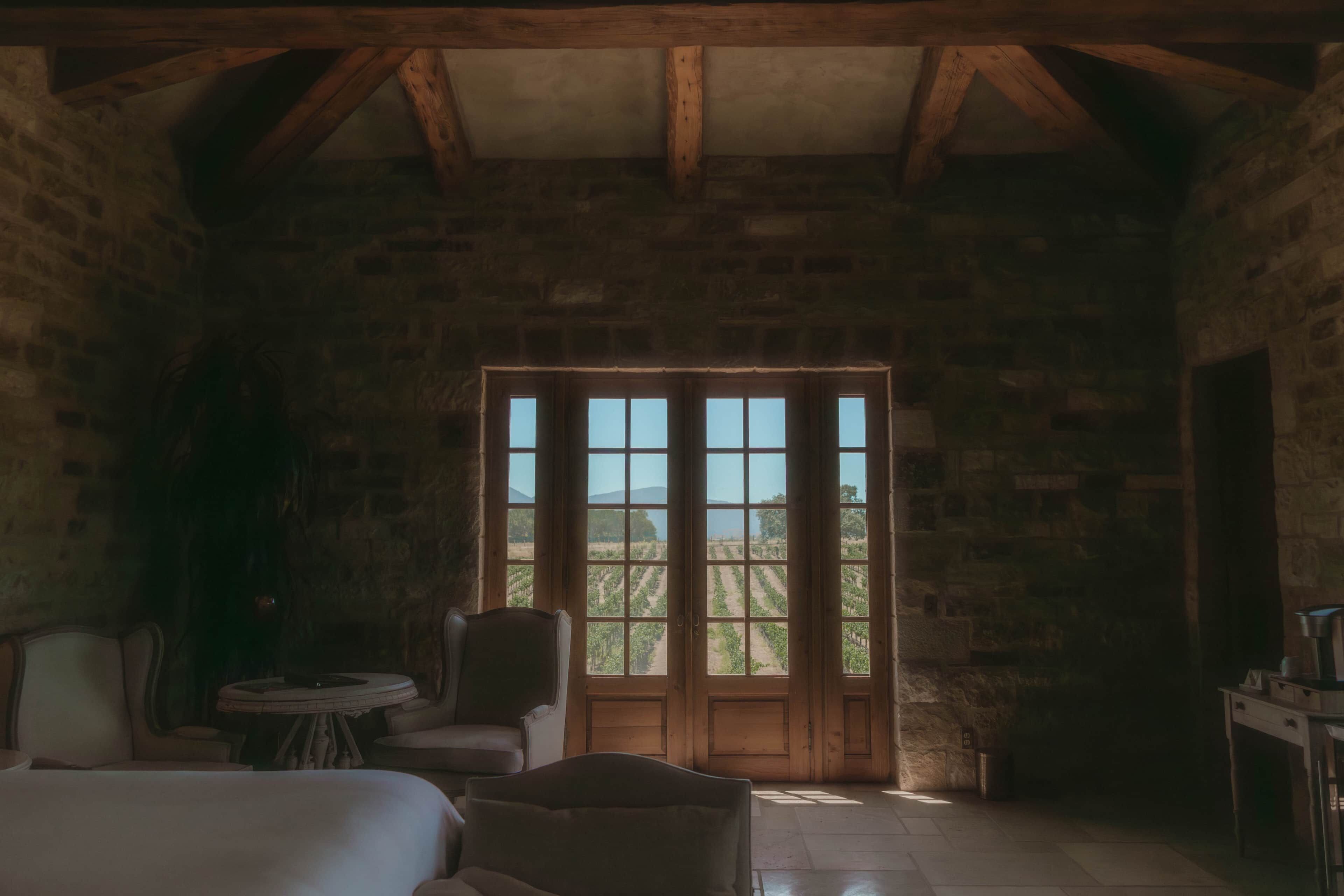 A rustic room with a large wooden door, a bed, a chair, and a small table.