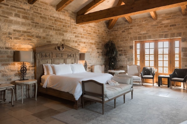 Une chambre à coucher de style traditionnel, avec un grand lit, une tête de lit en bois, une petite table, une chaise et une fenêtre laissant entrer la lumière naturelle.