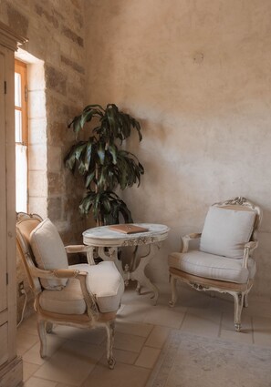 A room with two antique-style chairs, a small round table, and a large potted plant.