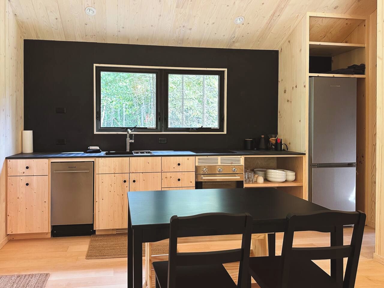 A compact kitchen with wooden cabinets, a built-in oven, a refrigerator, and a window overlooking greenery.