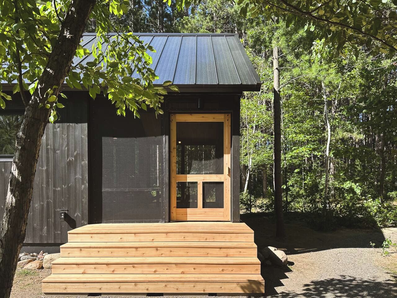 A small wooden cabin with a metal roof, a wooden door, and a set of wooden steps leading to the entrance.