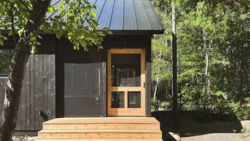 A small wooden cabin with a metal roof, a wooden door, and a set of wooden steps leading to the entrance.