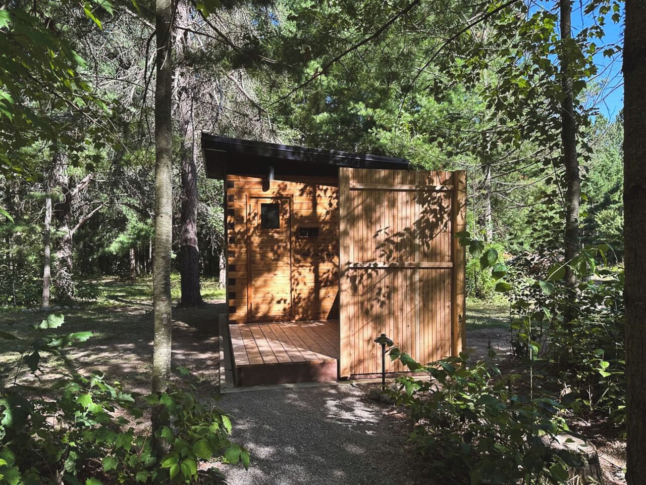 A small wooden cabin with a wooden door and a small window, surrounded by trees.