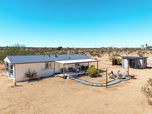 A single-story house with a covered patio area, a small adjacent shed, and a desert landscape in the background. - Beyond Horizon, Private Casita, Stargazing & Fast WiFi (Joshua Tree)