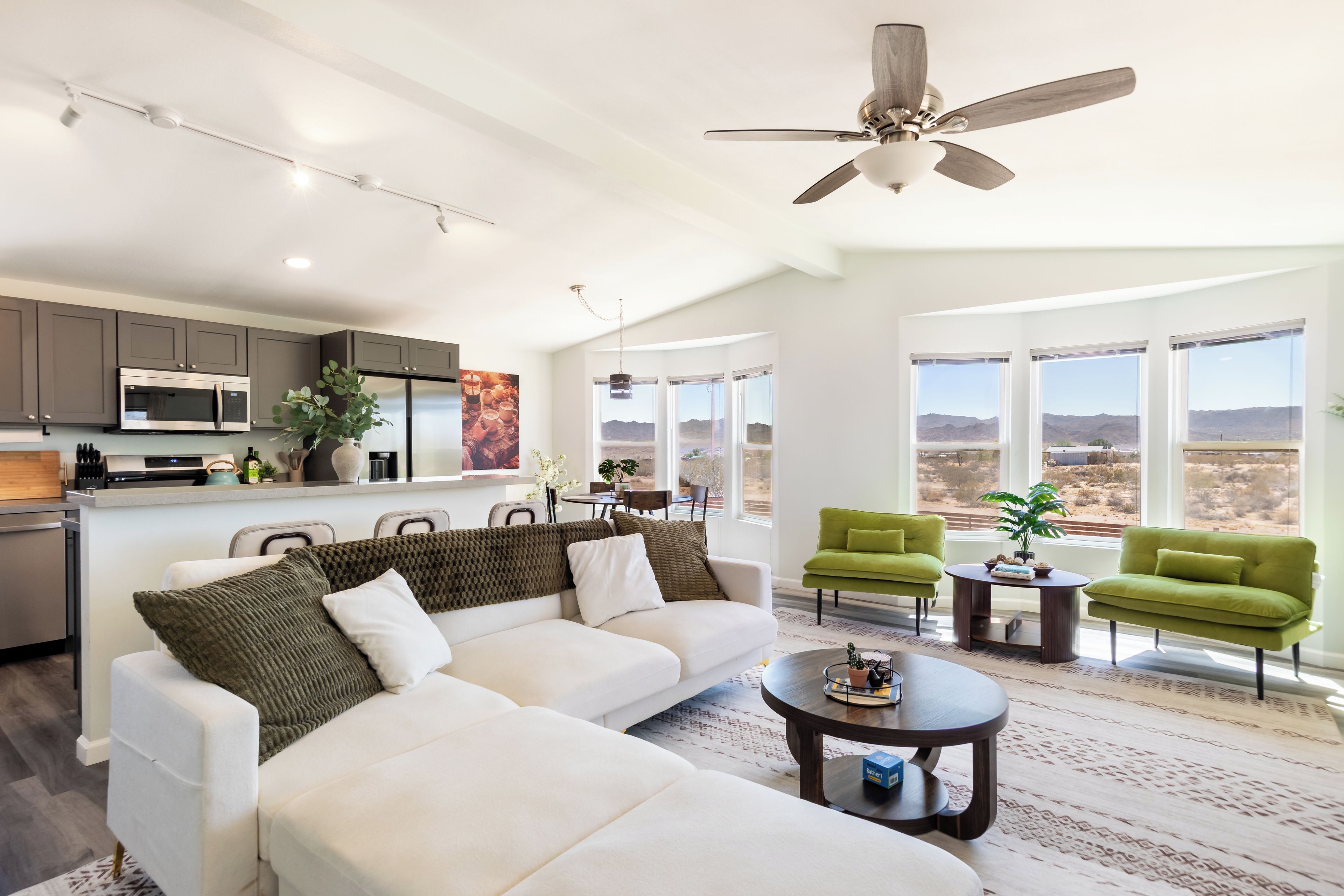 A modern living room with a white sofa, green armchairs, and a ceiling fan.