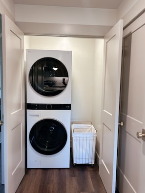 Una sala de bugaderia amb una rentadora i assecadora apilades, un tendero metàl·lic i un safataire blanc.