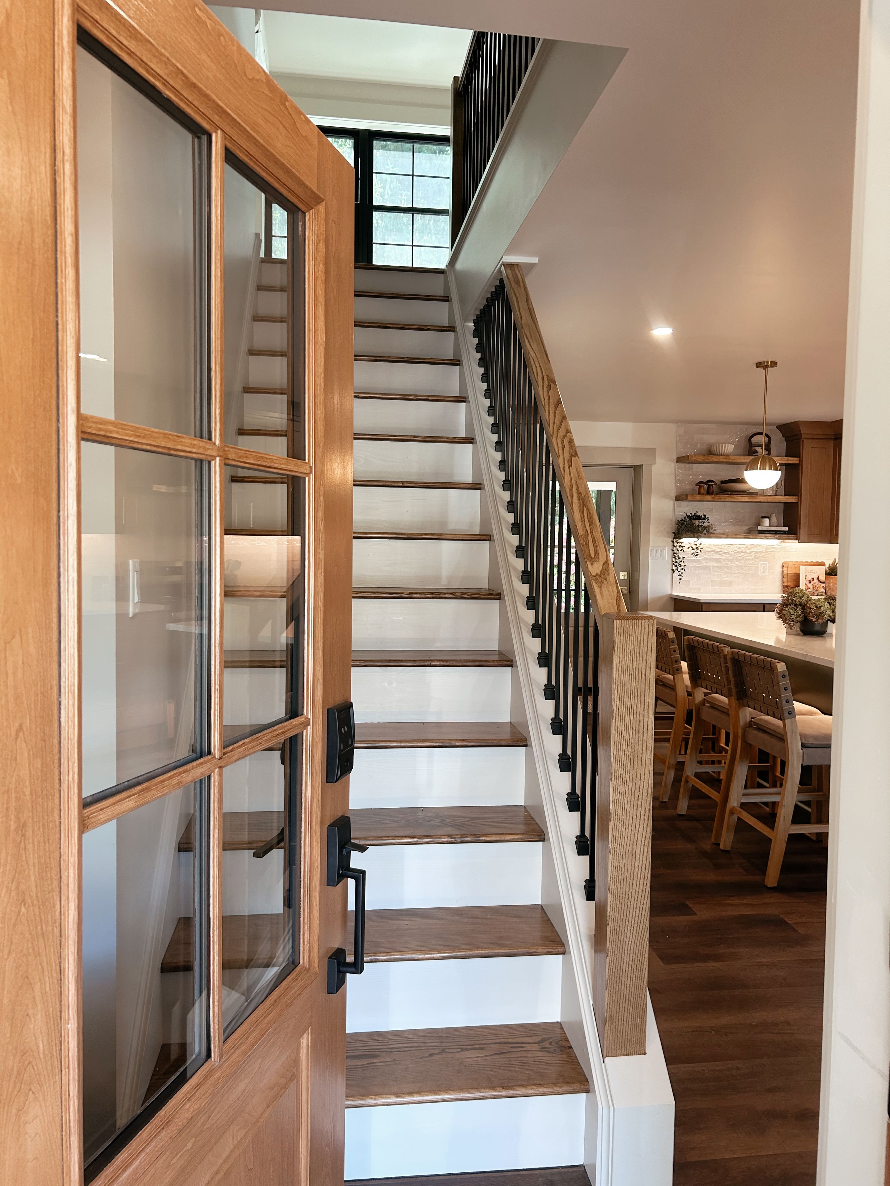 Eine Treppe mit Holzboden und einer Glastür links, die zu einem Küchenbereich mit Holzsesseln und einer Theke führt.