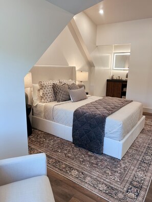 Een slaapkamer met een bed, nachtkastjes, een spiegel en een vloerkleed.