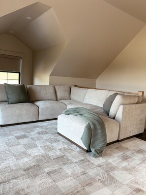 Een moderne woonkamer met een hoekbank, een kamerbreed tapijt en een schuine kap.