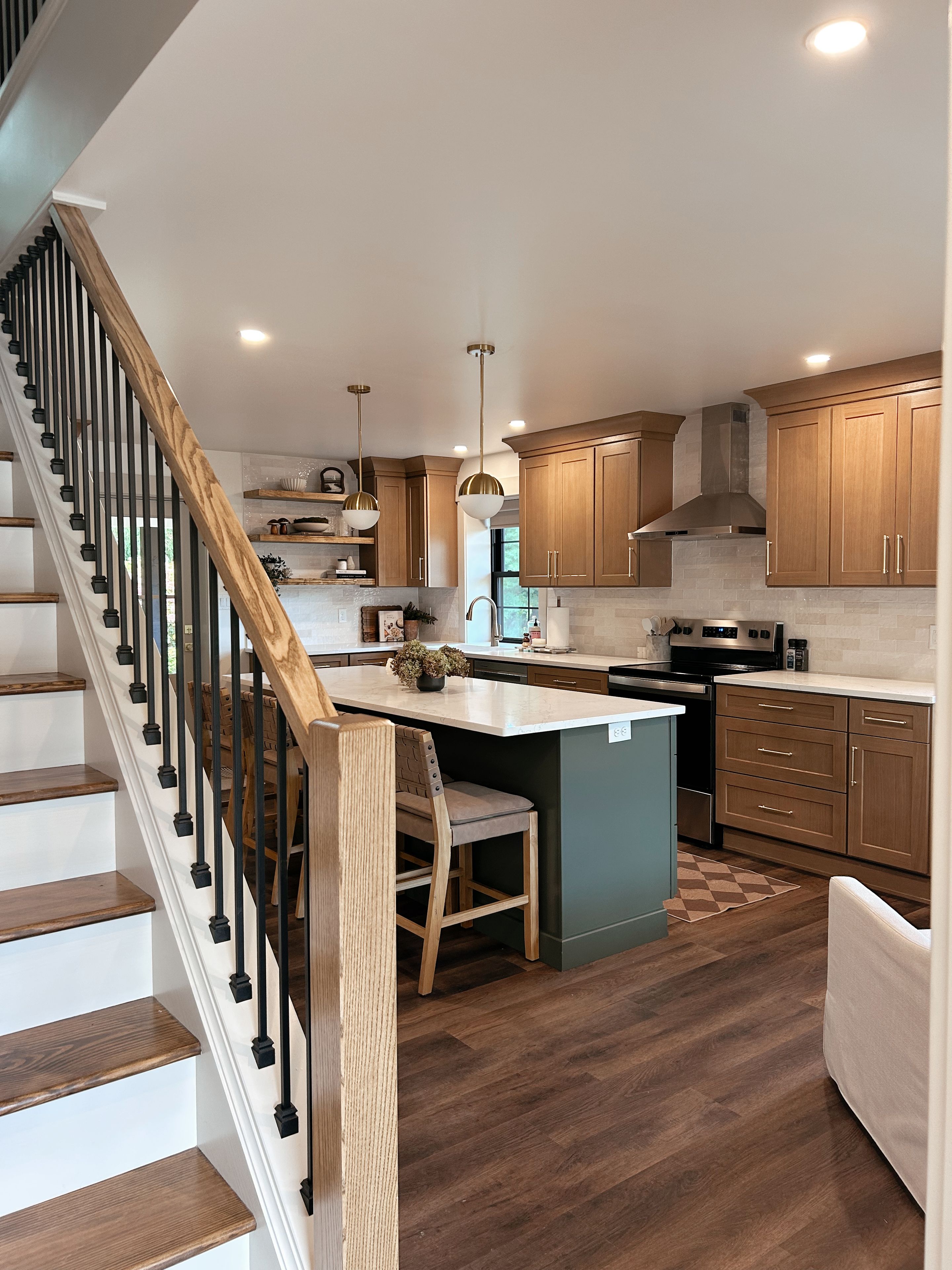 A modern kitchen with a central island, wooden cabinets, and a staircase with a wooden railing.