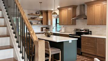 A modern kitchen with a central island, wooden cabinets, and a staircase with a wooden railing.
