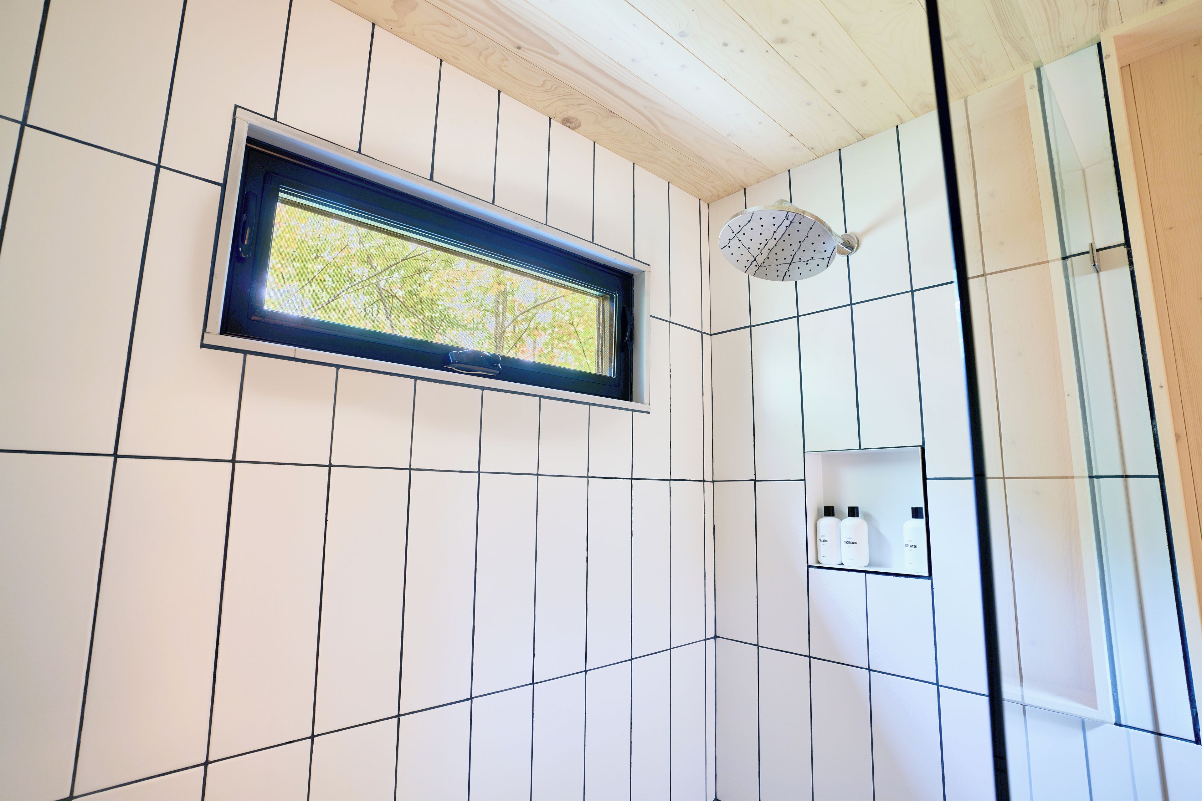 Une salle de bain avec une fenêtre, une douche et une étagère où sont rangés les articles de toilette.
