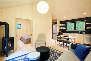 A compact living space with a wood-paneled interior, a fireplace, a dining area, and a kitchen with a large window. - Scandi Spruce Cabin in the Woods #2 (Grand Rapids)