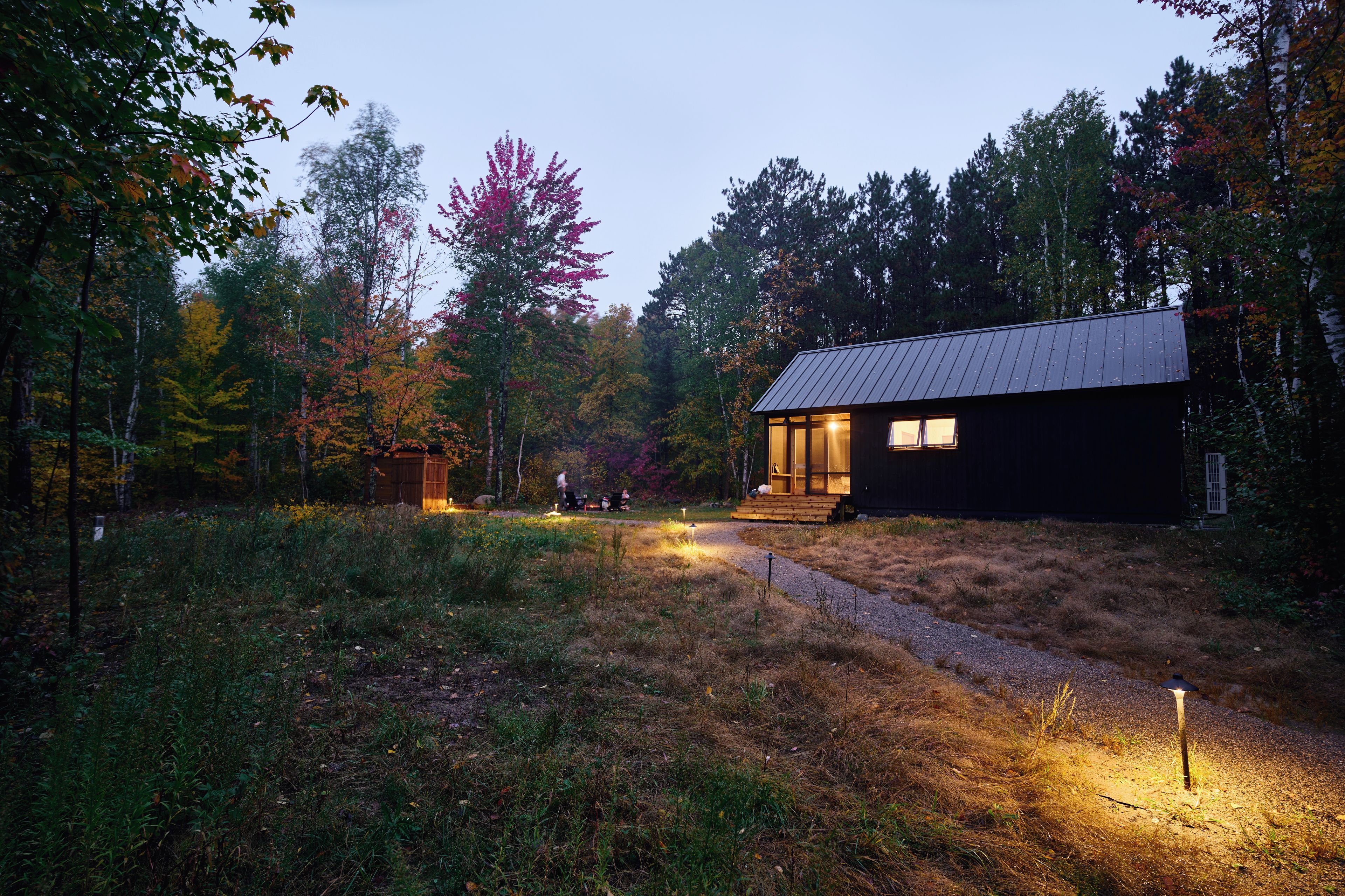 Une cabane surmontée d’un toit en métal, entourée d’une forêt aux couleurs automnales.