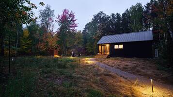Une cabane surmontée d’un toit en métal, entourée d’une forêt aux couleurs automnales.