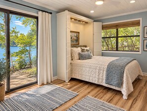 Een slaapkamer met een groot raam, een bed met een beddegoed met een patroon en uitzicht op een meer.