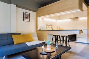 Ein modernes Wohnzimmer mit einer Couch, einem Couchtisch und einer Küchenzeile mit Barhocker.