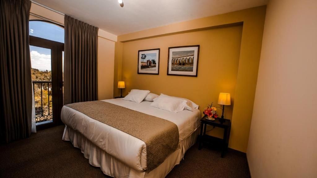 A hotel room with a bed, two bedside lamps, a nightstand, and a window with curtains.