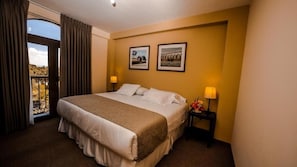 Una habitación de hotel con cama, dos lámparas de noche, una mesita de noche y una ventana con cortinas.