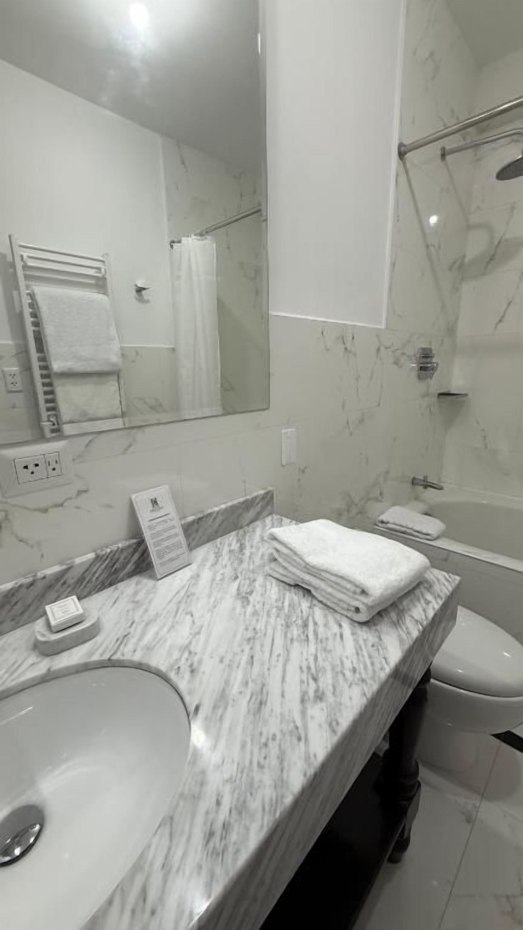A bathroom with a marble sink, a mirror, a towel rack, and a shower area.