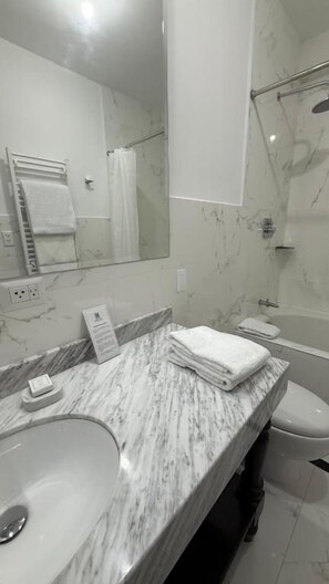 Un baño con lavamanos de mármol, un espejo, toallero y cabina de ducha.