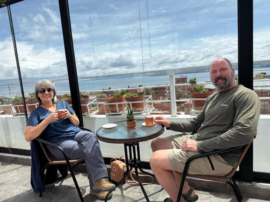 Two people seated at a round table with a view of a body of water and buildings in the background.