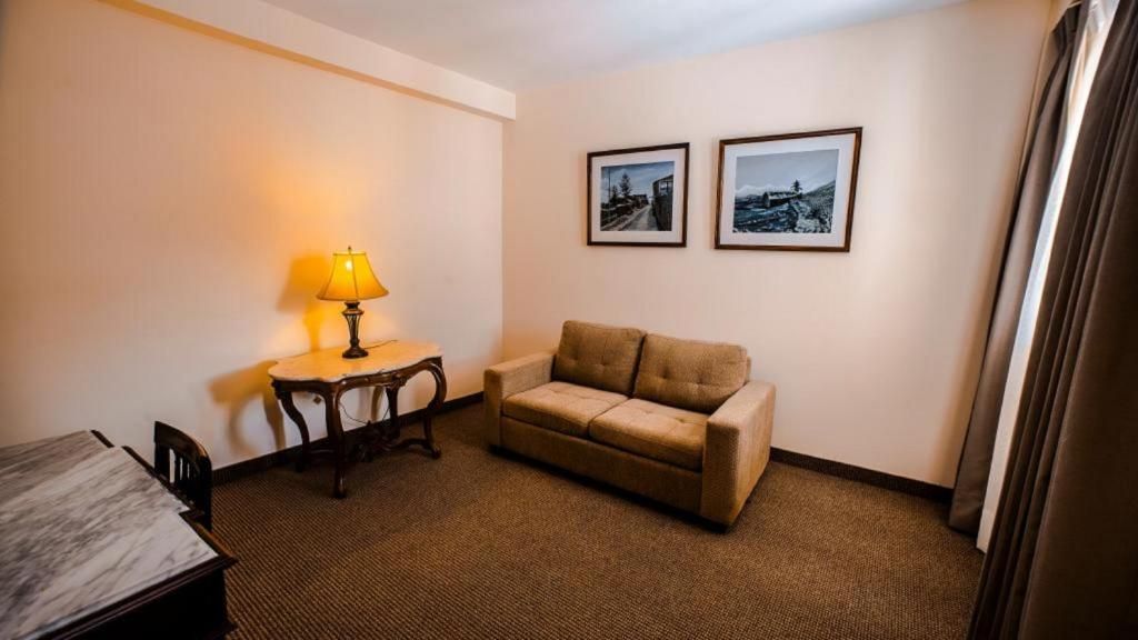 A hotel room with a sofa, a small table with a lamp, and two framed pictures on the wall.
