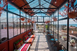 A covered outdoor seating area with tables and chairs, a bench with colorful cushions, and hanging plants. - Atojja Chucuito Hotel (Chucuito)