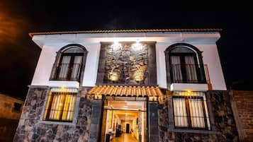 Un edificio de dos pisos con fachada de piedra, techo de tejas y entrada central con puerta de cristal.
