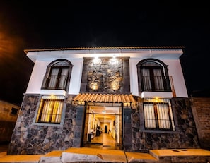 Un edificio de dos pisos con fachada de piedra, techo de tejas y entrada central con puerta de cristal.