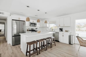 A modern kitchen with white cabinetry, stainless steel appliances, and a central island with stools. - Terra Aura: Tempe Home with Pool & Spa (Tempe)