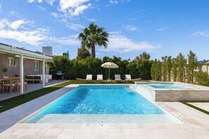 Une piscine rectangulaire divisée en deux zones distinctes, entourée d’un patio aménagé avec des chaises longues et un espace salon couvert.