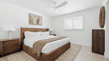 A bedroom with a bed, nightstands, a ceiling fan, a window with blinds, and a wall-mounted artwork.