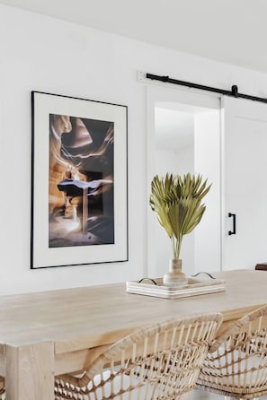 A modern dining area with a wooden table, wicker chairs, a framed artwork, and a potted plant. - Terra Aura: Tempe Home with Pool & Spa (Tempe)