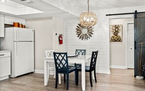 Cozinha moderna com geladeira branca, mesa de jantar com cadeiras, um objeto decorativo na parede e extintor de incêndio.