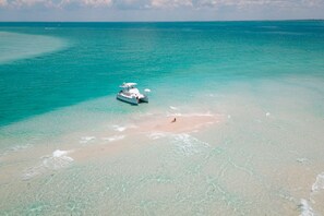 A boat on a turquoise sea with a sandy beach in the foreground. - 5 Stars~WALK TO BEACH from Serendipity Suites! 2-of-2  2-bed/2-ba Cottage Suites (Holmes Beach)