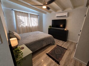 A bedroom with a bed, a TV, a ceiling fan, and a window with curtains. - Spacious 4-bedroom cozy cottage (Albuquerque)