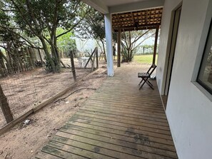 A wooden deck leading to a covered patio area with a single chair. - House for 6 People - Recanto dos Eucaliptos - Great location - Pet Friendly (Imbituba)
