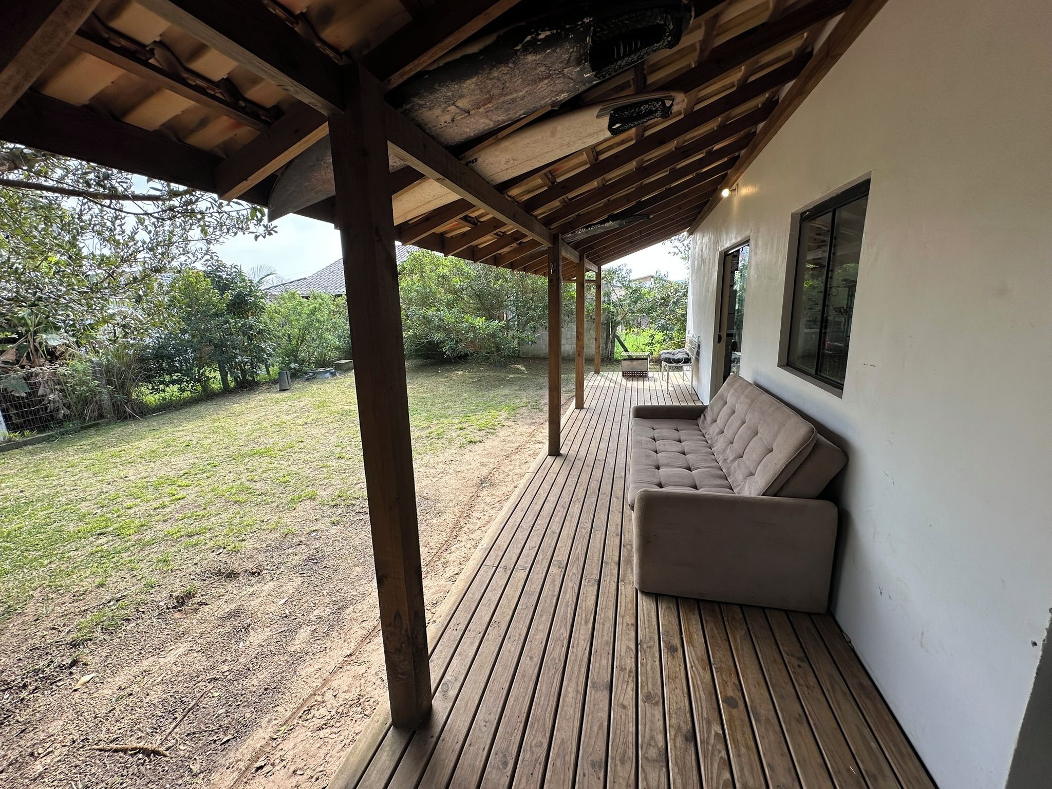 A covered patio area with a wooden deck, a beige sofa, and a view of a garden.