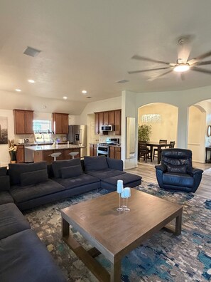 A modern living room with a sectional sofa, a coffee table, and a dining area with a chandelier. - Spacious, bright & modern 3BR+ office in a very safe neighborhood with lakes. (Houston)